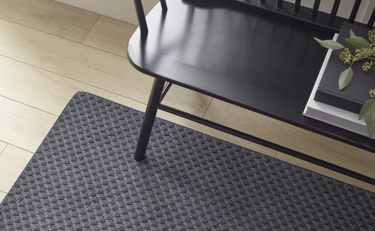 black textured area rug over light natural hardwood floors in entry way with black bench